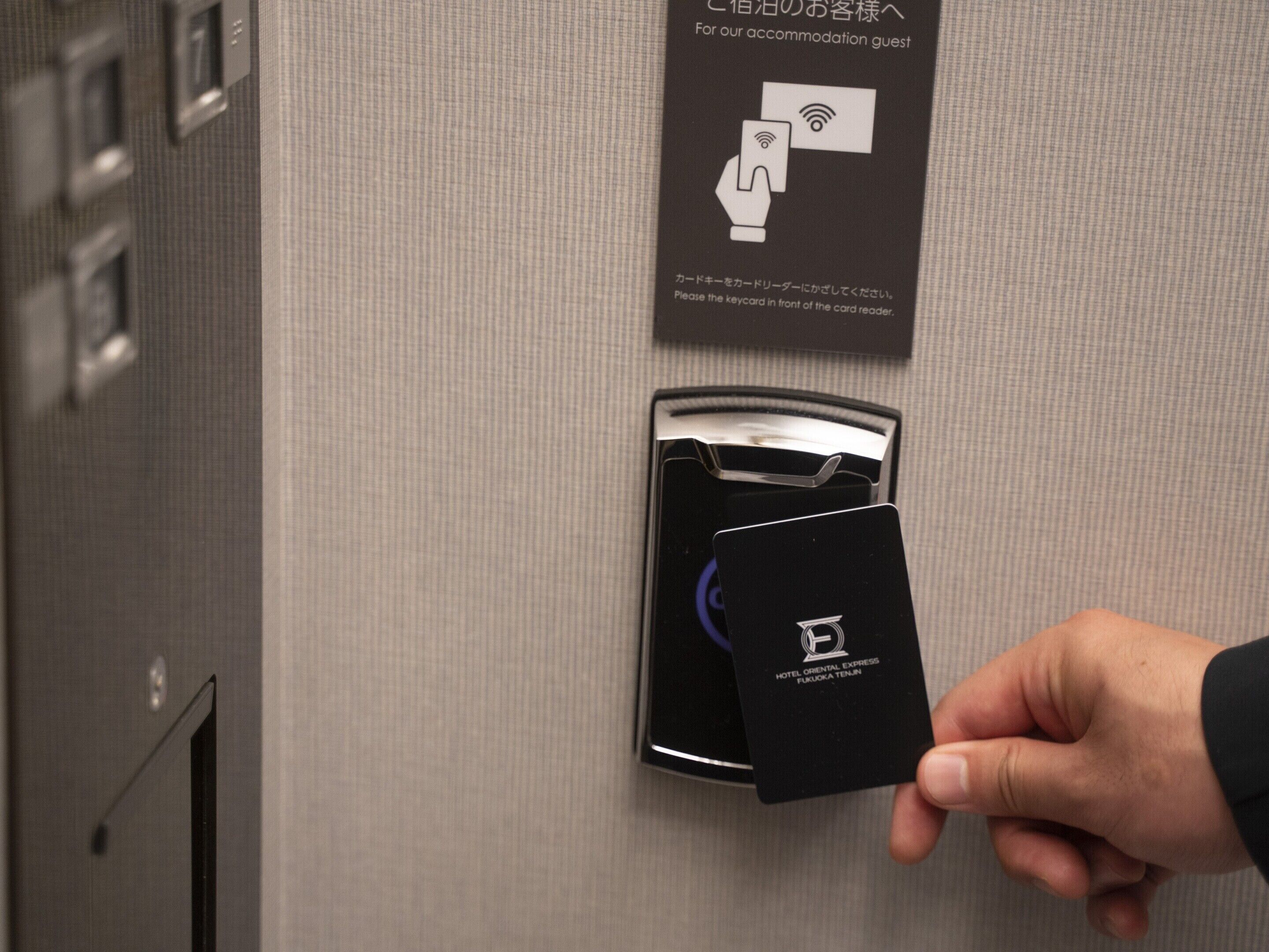 Une main tenant une carte près d’un lecteur de cartes, avec un panneau indiquant qu’il faut placer la carte devant le lecteur.