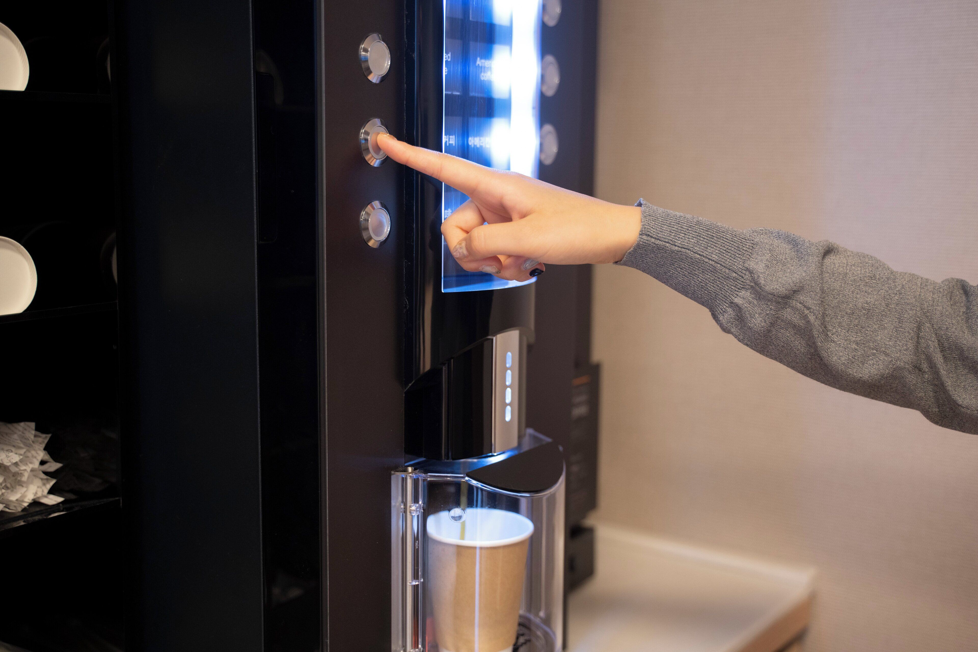 A hand pressing a button on a coffee machine with a cup dispenser below.
