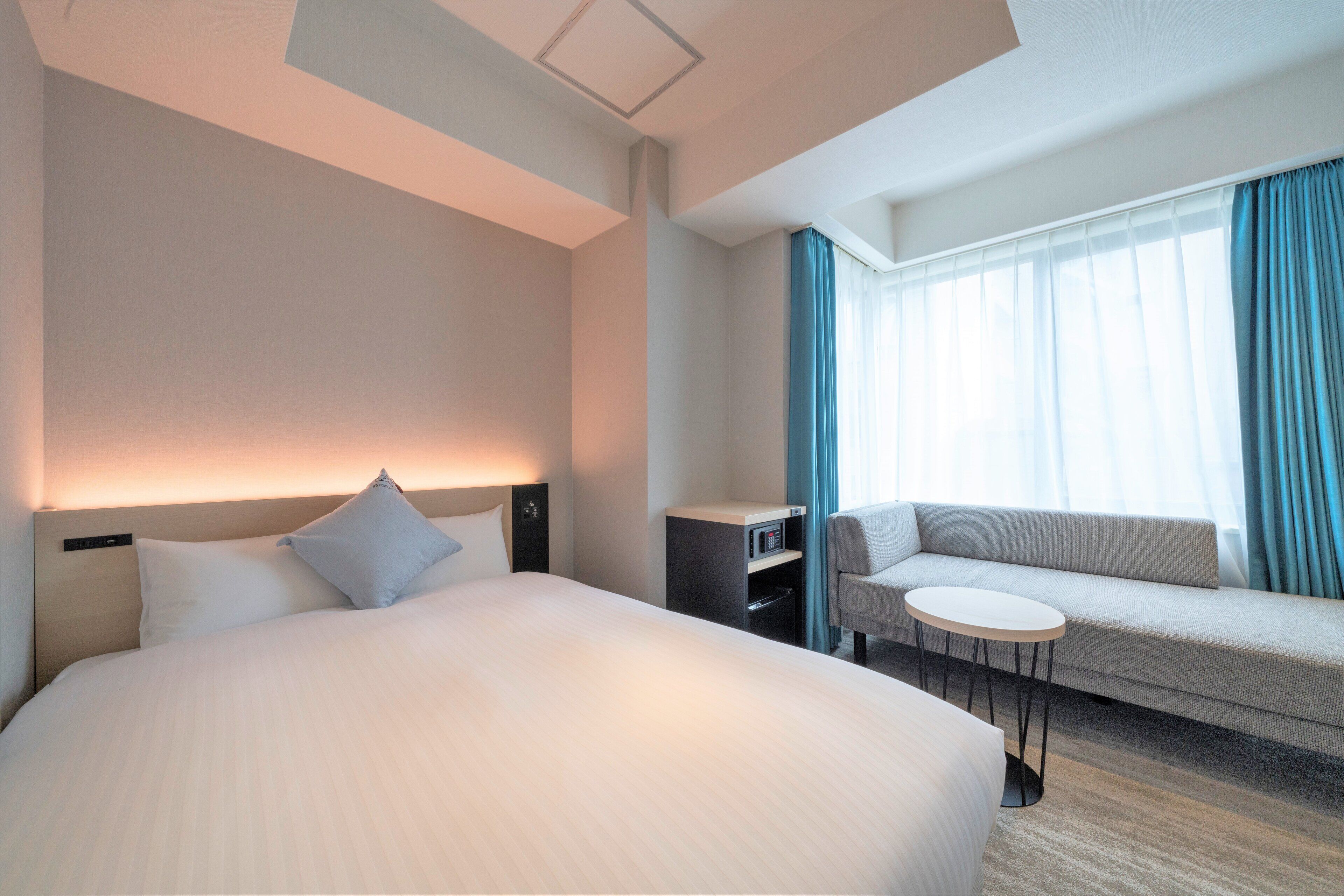 A modern hotel room with a large bed, a sofa, a small table, and a desk with a computer.