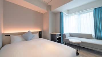 A modern hotel room with a large bed, a sofa, a small table, and a desk with a computer.