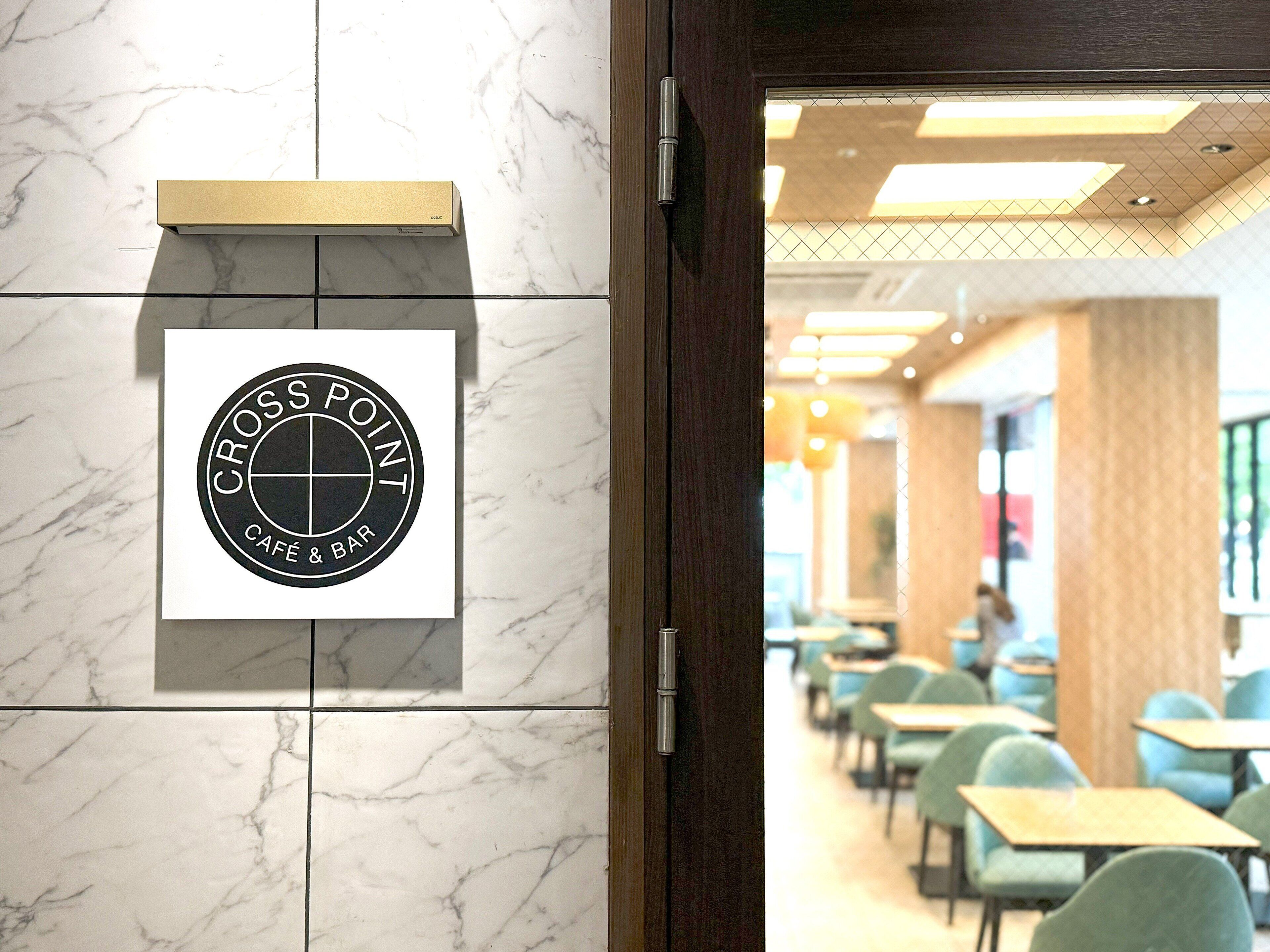 A café and bar sign on a marble wall, a wooden door, and a seating area with tables and chairs.