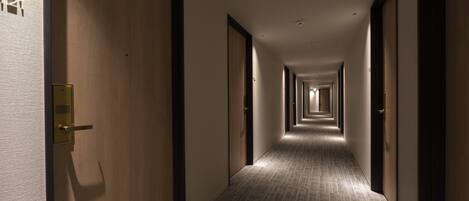 A hotel hallway with wooden doors, a carpeted floor, and a series of lights along the ceiling.