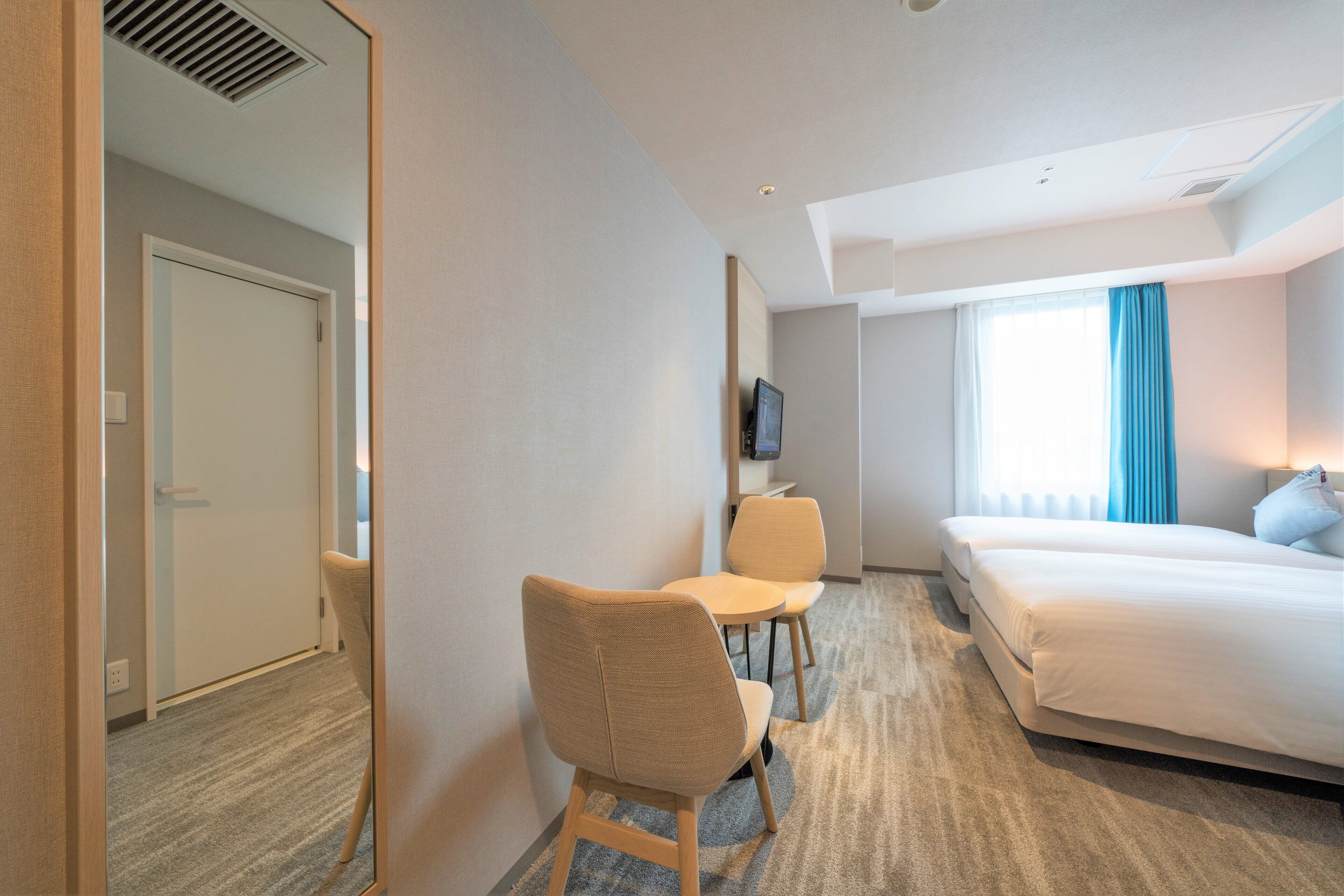 A hotel room with a bed, a desk with a chair, a television, and a window with curtains.