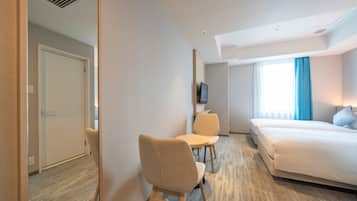 A hotel room with a bed, a desk with a chair, a television, and a window with curtains.