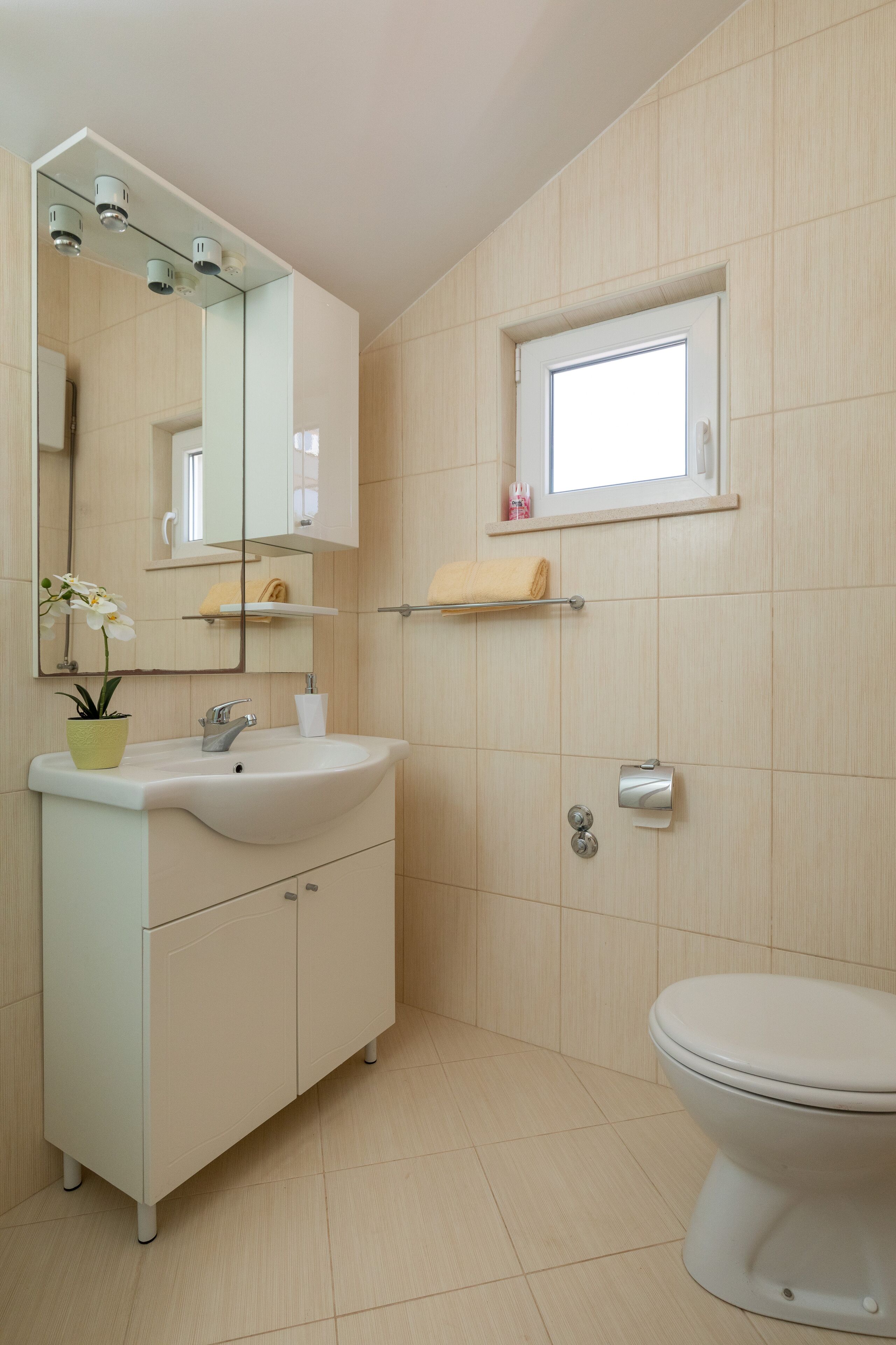 A modern bathroom with a sink, mirror, toilet, and a small window.