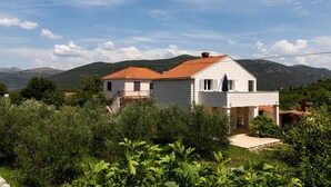 A two-story house with a red-tiled roof, surrounded by greenery and mountains in the background. - Apartment Relax Ston (Ston)