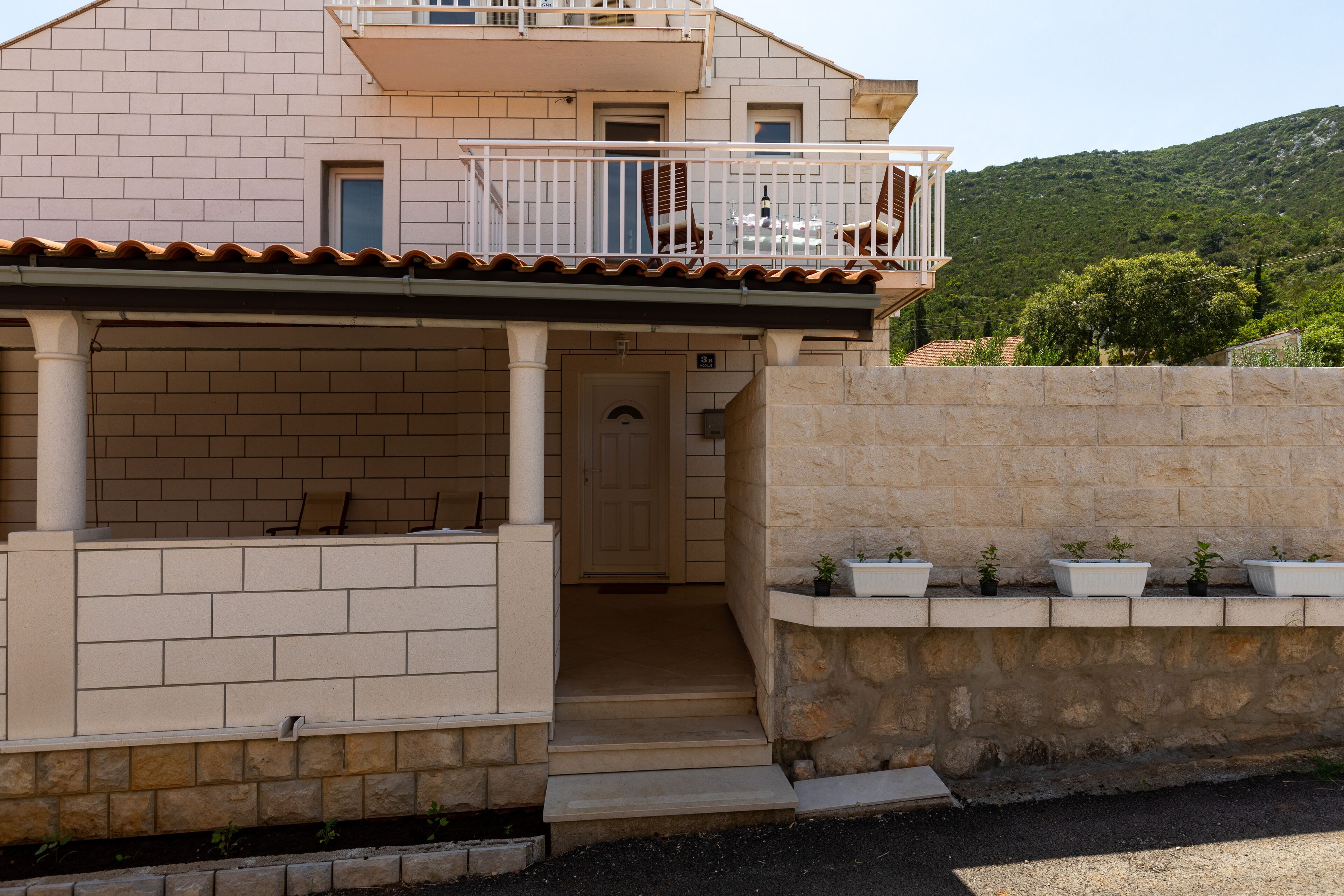 Un bâtiment à deux étages doté d’un balcon, d’une porte et d’un petit espace porche agrémenté de plantes en pot.