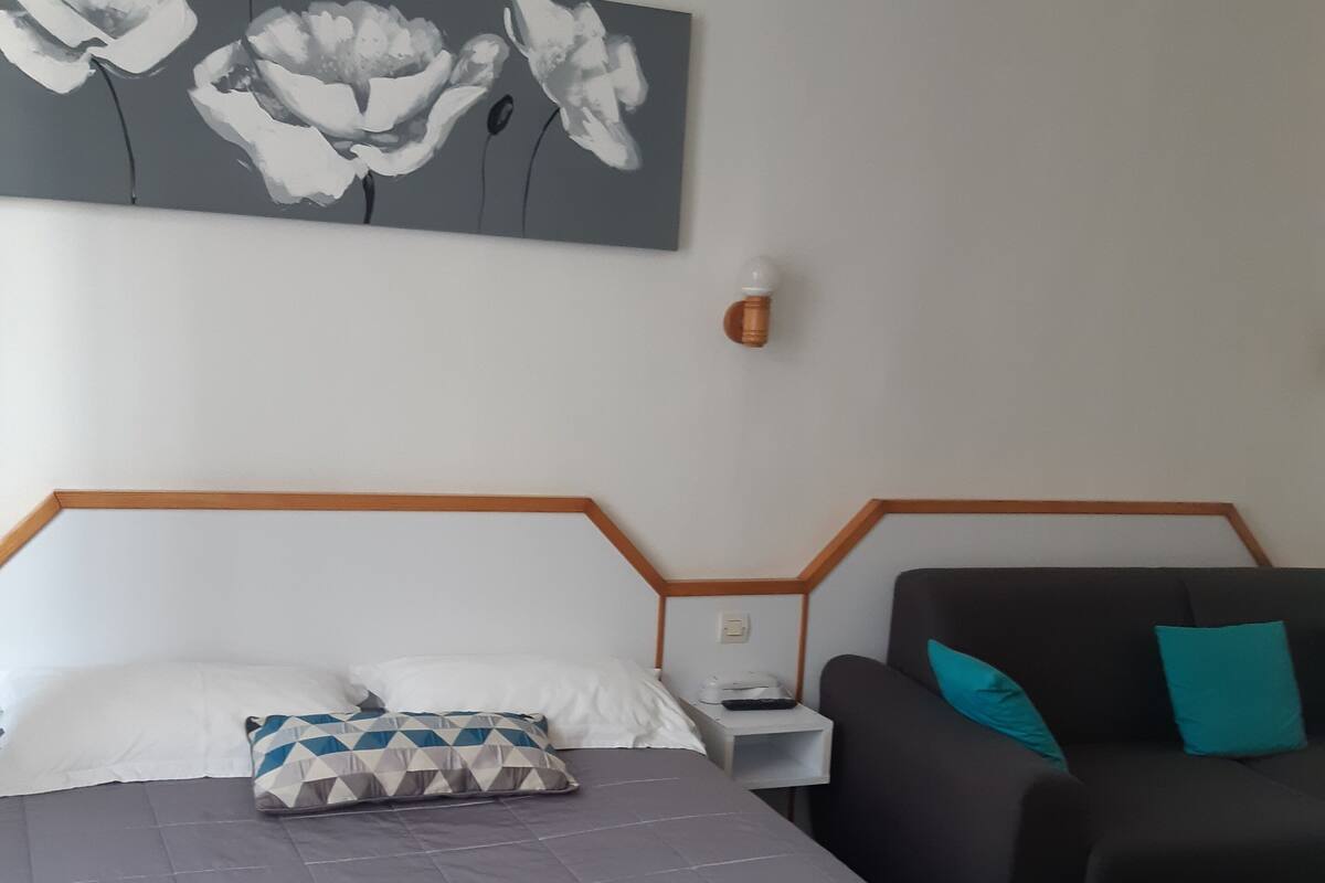 A hotel room with a bed, a nightstand, a lamp, and a sofa.