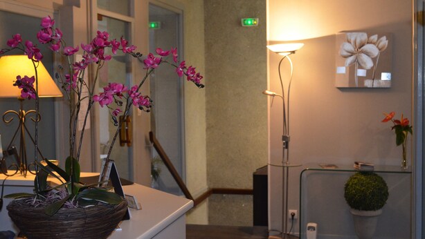 A reception area with a reception desk, a standing lamp, a wall-mounted flower painting, and a potted plant. - Hotel de La Croix de Malte (Cherbourg-en-Cotentin)