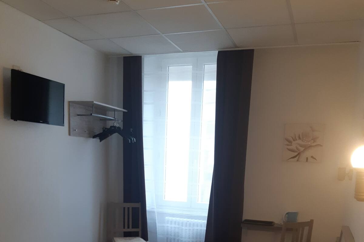 A hotel room with two beds, a TV mounted on the wall, a small table, and a window with curtains.