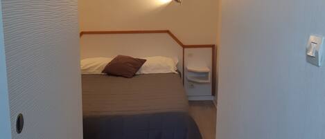 A bedroom with a bed, a nightstand, a wall-mounted light, and a painting.
