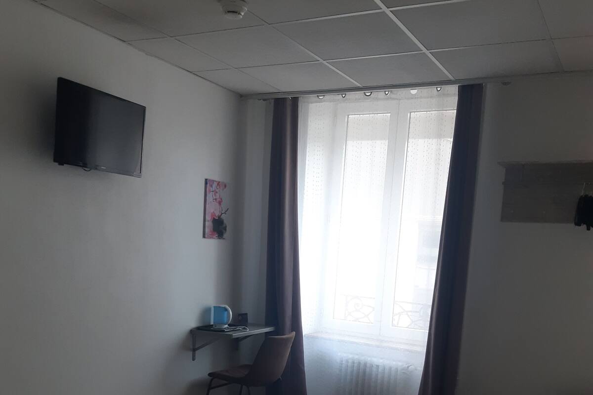 A hotel room with a bed, a desk with a chair, a television mounted on the wall, and a window with curtains.