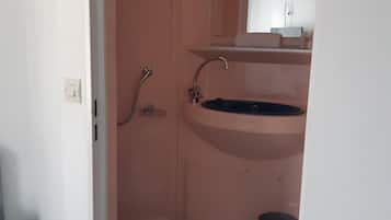 Un baño pequeño y estrecho con un lavamanos, un espejo encima y una zona de ducha.