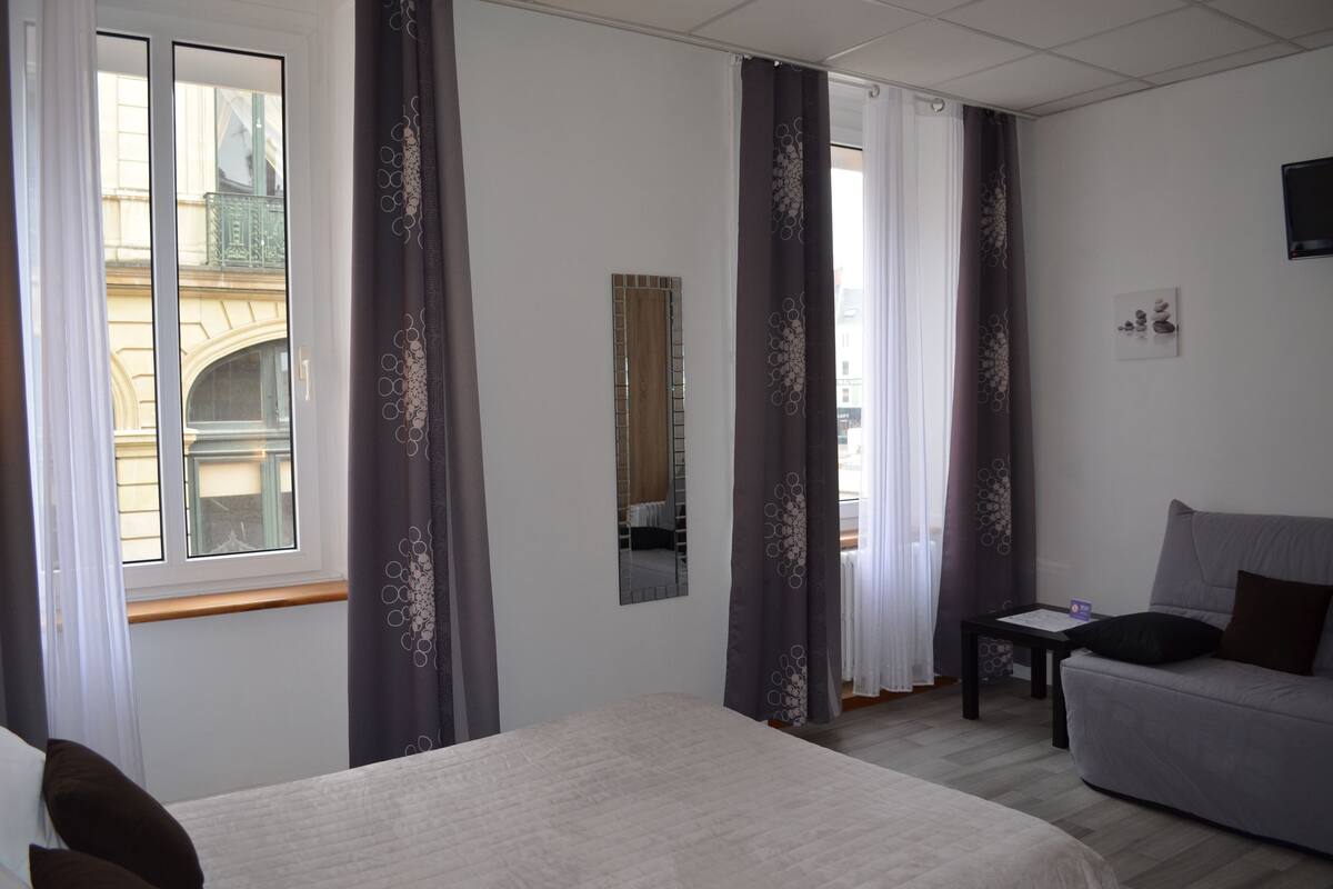 A hotel room with a bed, a sofa, a small table, and a mirror.
