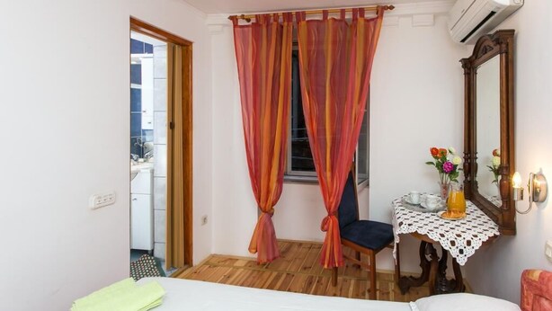 Un dormitorio con una cama, una mesita con un florero y un espejo en la pared.