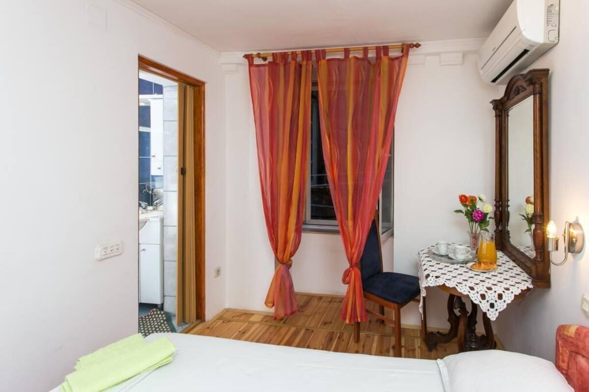 Ein Schlafzimmer mit einem Bett, einem kleinen Tisch mit Blumen und einem Spiegel an der Wand.