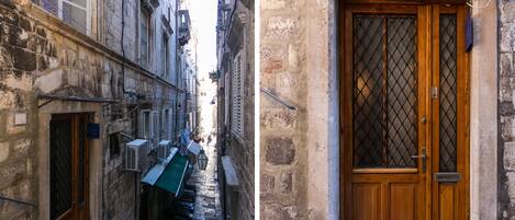 Un callejón estrecho con una puerta de madera y una ventana con reja de metal.