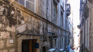 Una estrecha calle empedrada flanqueada por edificios históricos, con unidades de aire acondicionado y una puerta de madera.