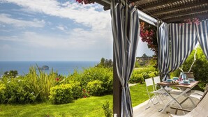 An outdoor patio with a table set for two, overlooking a lush garden and the sea. - Villa Le Rondini - Two Bedroom Villa, Sleeps 4 (Ionian Islands)