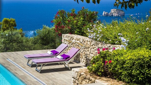 A poolside area with two sun loungers, a stone wall, and a view of the sea. - Villa Le Rondini - Two Bedroom Villa, Sleeps 4 (Ionian Islands)