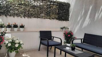 Un patio con una pared cubierta de follaje, varias plantas en macetas y dos sillas negras con una pequeña mesa.