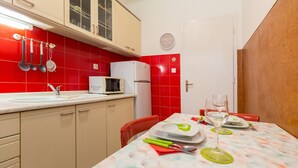 Cocina compacta con microondas, refrigerador y utensilios colgantes. Una mesa de comedor con platos y cubiertos dispuesta para dos.