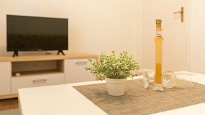 Una sala de estar moderna con un televisor de pantalla plana sobre un mueble de madera, una planta en maceta y una botella de vidrio alta sobre una mesa texturizada.
