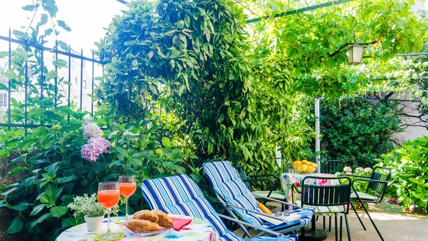 Un espacio exterior con sillones a rayas, una mesa con mantel floral y una planta en maceta.