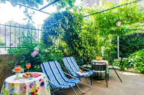En uteplats med två randiga solstolar, ett bord med ett blommigt bordsduk och ett glas att dricka ur.