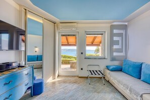 A modern room with a sofa, a television, a dresser, and a view of the sea.
