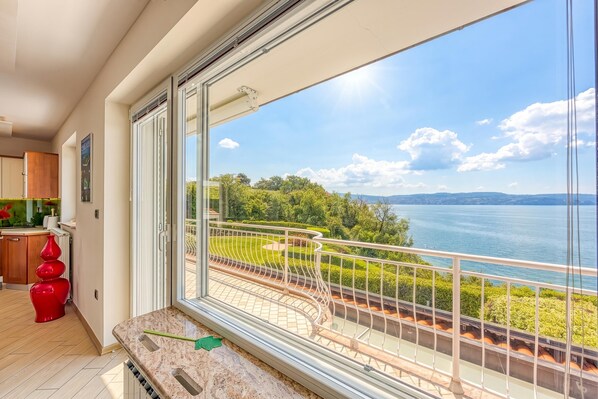 Un balcon avec vue sur un lac, un coin repas agrémenté d’un vase rouge et une cuisine avec des meubles en bois.