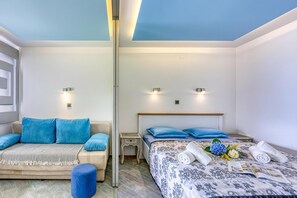 A bedroom with a sofa, a bed with a patterned bedspread, and two bedside tables with lamps.