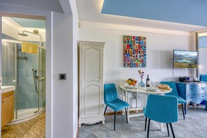 A modern room with a glass shower, a white cabinet, a dining table with chairs, and a colorful artwork on the wall.