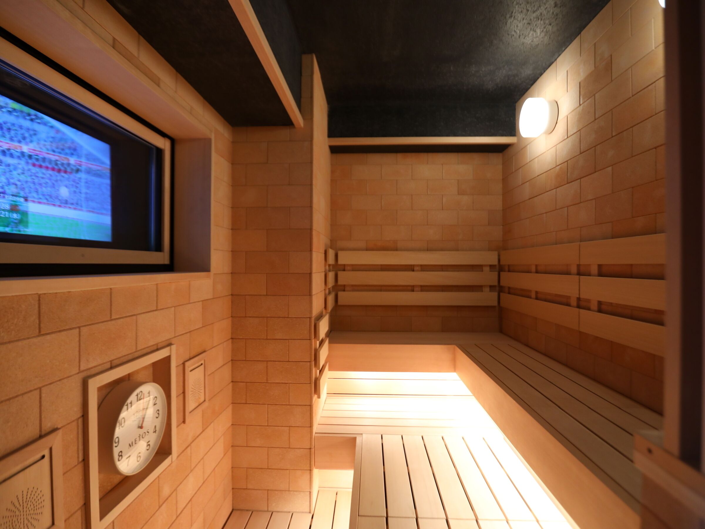 A sauna with wooden benches, a clock, and a television screen displaying a sports event.