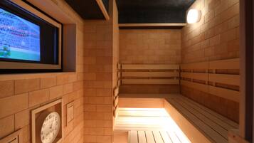 A sauna with wooden benches, a clock, and a television screen displaying a sports event.