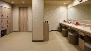 A modern bathroom with a checkered wall pattern, wooden cabinets, a large mirror, and a clock. - Dormy Inn Ikebukuro Hot Springs (Tokyo)