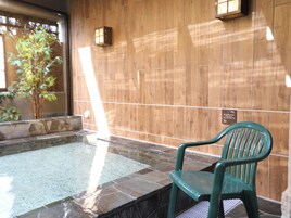 A wooden wall with a tiled floor, a green plastic chair, and a small tiled hot tub.