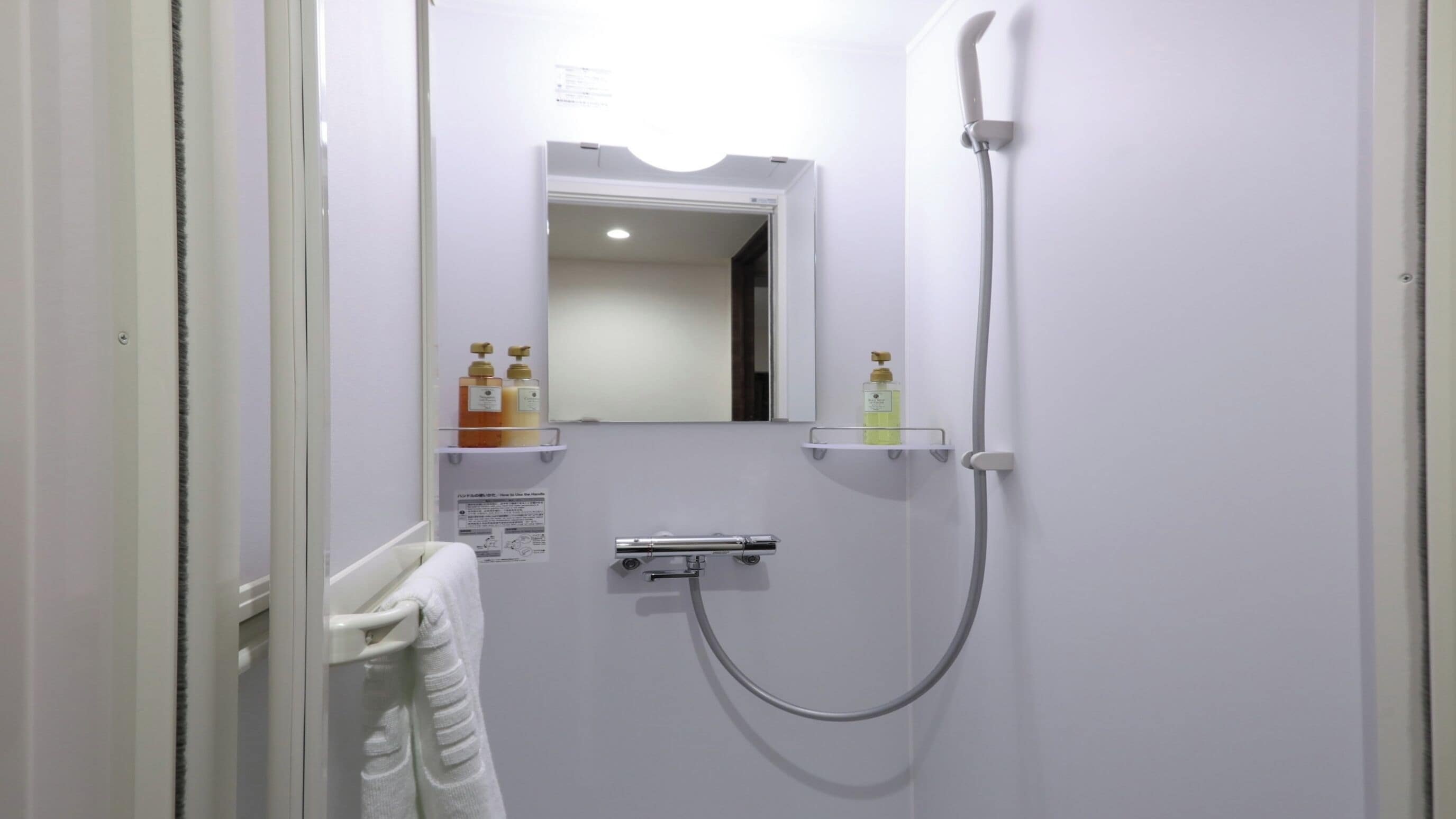 A bathroom with a shower, a towel rack, and two bottles of soap on a shelf.