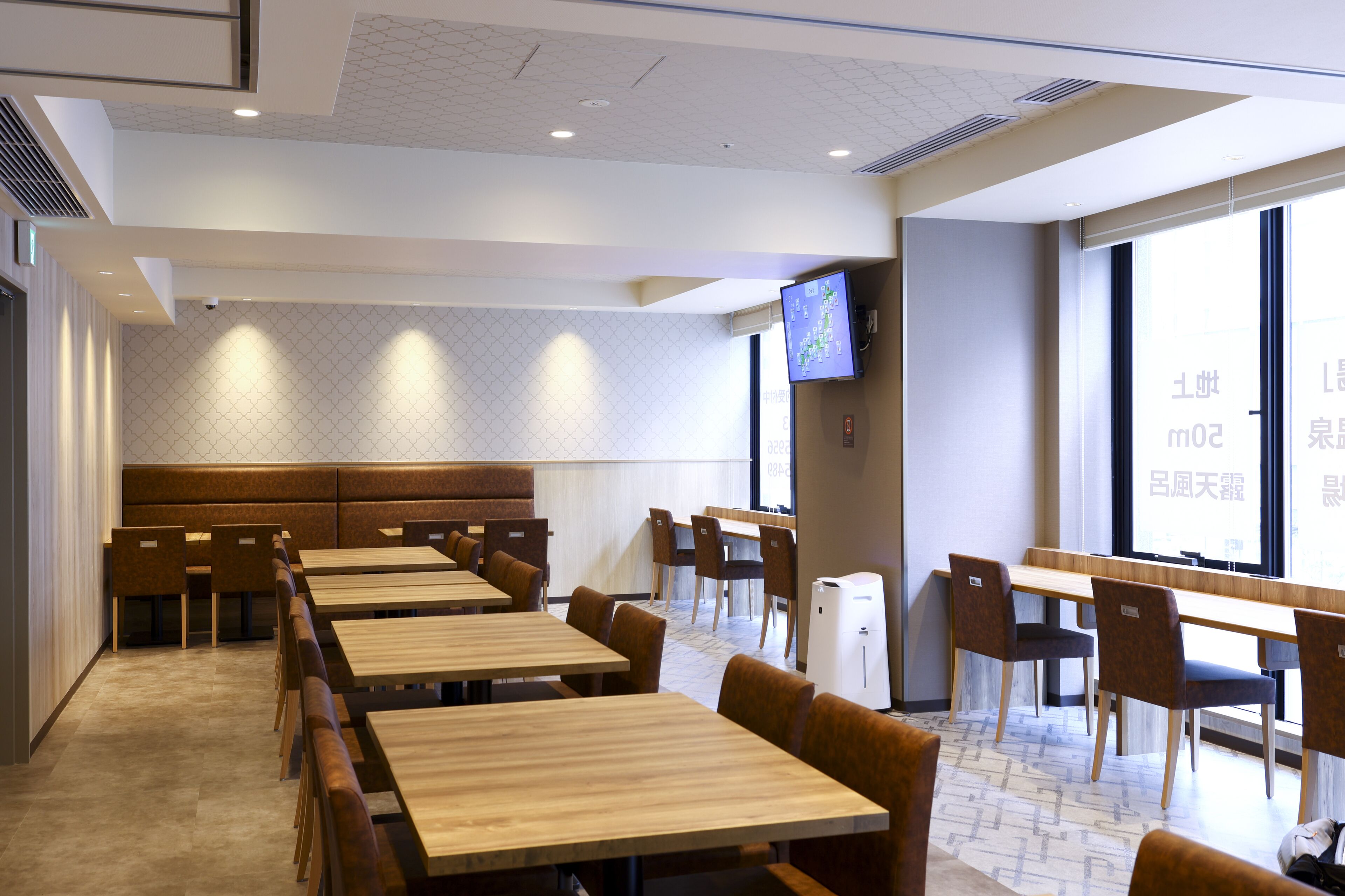 A modern dining area with wooden tables and chairs, a large window with a view, and a television mounted on the wall.