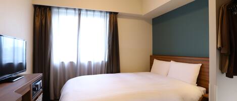 A hotel room with a bed, a TV on a wooden dresser, and a window with curtains.