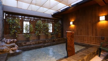 Um interior em estilo tradicional japonês, com um elemento de água em pedra, plantas de bambu e paredes de madeira.