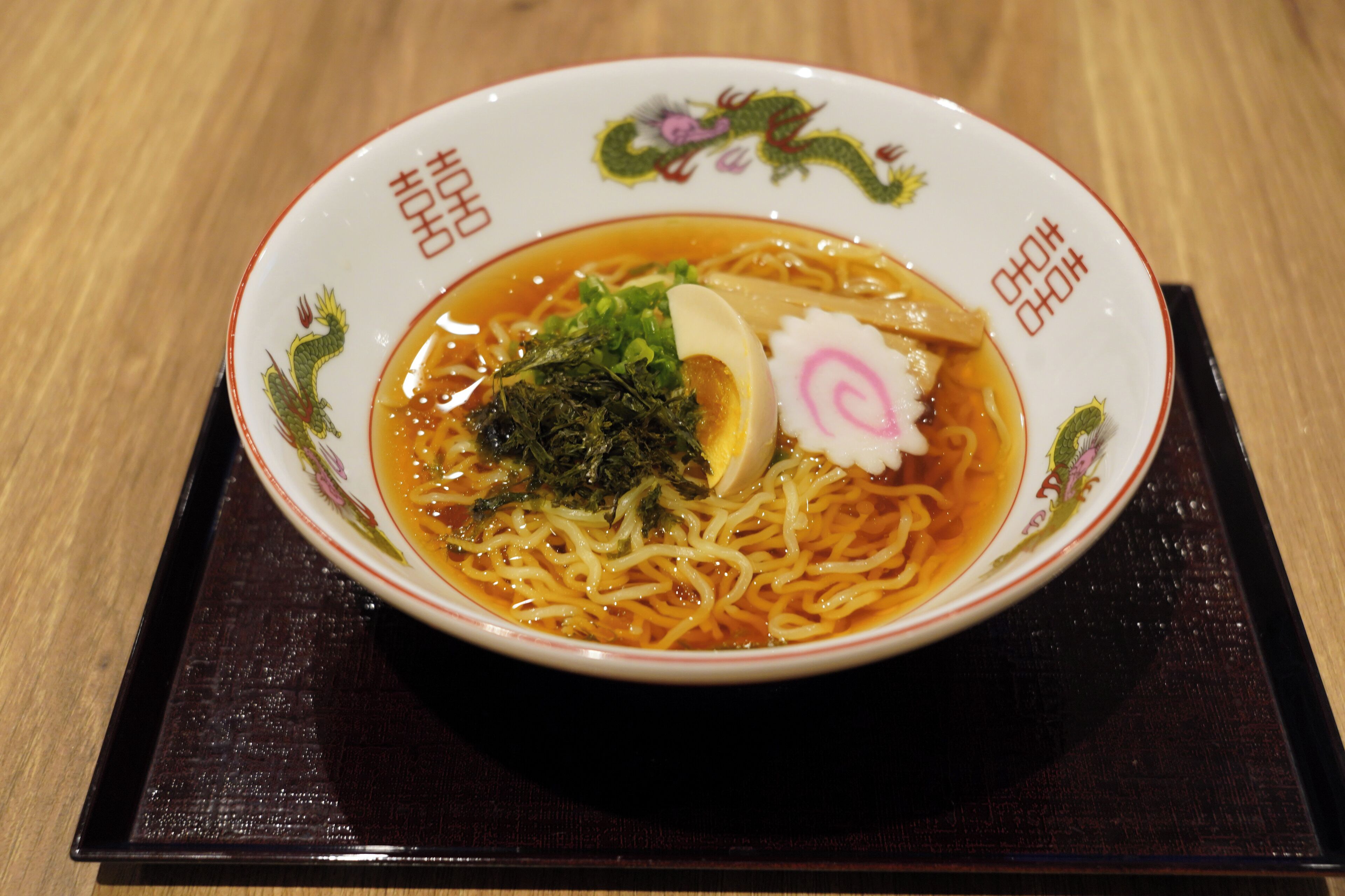 A bowl of ramen with seaweed, egg, and a pink garnish on a decorative plate.