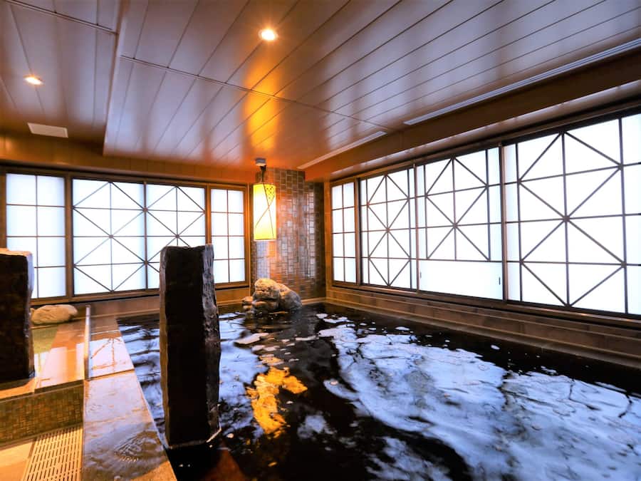 Une pièce de style japonais traditionnel, avec un sol recouvert de tatamis, une fontaine en pierre et de grandes fenêtres à carreaux.
