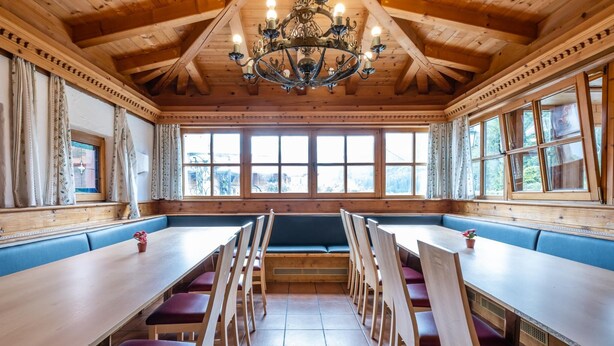 Un espace repas avec des tables et des bancs en bois, un lustre et de grandes fenêtres.