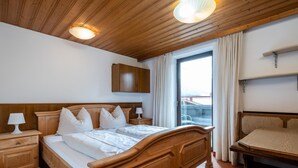 Une chambre d’hôtel avec un lit en bois, une table de chevet avec une lampe, une fenêtre avec des rideaux et un plafond avec des poutres et des luminaires en bois.