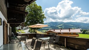 Une terrasse extérieure avec des tables et des chaises, un bâtiment en bois et une vue sur les montagnes.