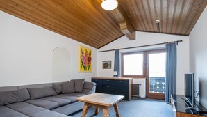 Un salon comprenant un canapé, une table basse en bois, un coin cuisine avec des placards, une fenêtre avec des rideaux et un téléviseur.