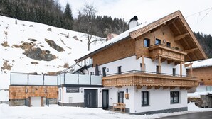 Perinteinen puinen alppimaja, jossa on parveke, kyltti, jossa lukee ”KOBELHAUSL Bei Haus”, ja lumipeitteinen maisema.