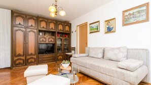A living room with a sofa, a glass coffee table, wooden cabinets, a television, and wall-mounted artwork. - Apartment Marina (Dubrovnik)