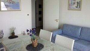 Ein Essbereich mit Tisch, Stühlen und einem Blumenstrauß. Ein blaues Sofa und eine Tür zu einem anderen Raum sind ebenfalls vorhanden.